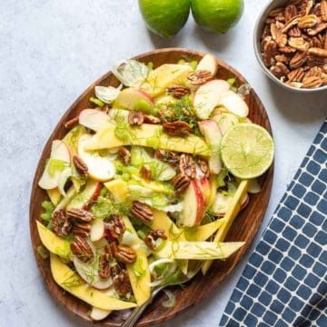 fennel salad on a brown plate with limes on the side