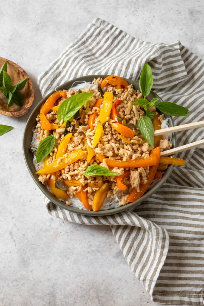 thai basil chicken with vegetables and rice noodles in a bowl with chopsticks